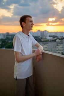 Man in white polo shirt standing on balcony in dusk