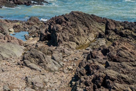 Craggy jagged shoreline with ocean in background on sunny day