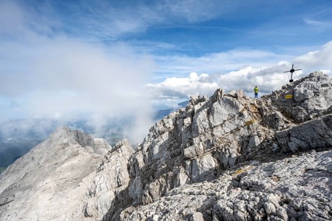 Mountaineer on the rocky summit of the Watzmann Mittelspitze with summit cross, Watzmann crossing,