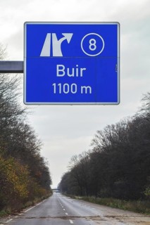 A traffic sign with a directional arrow points to the Buir motorway exit under a blue sky,