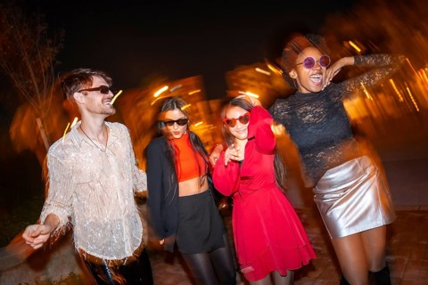 Night photo with flash and motion of four stylish friends dancing in the street