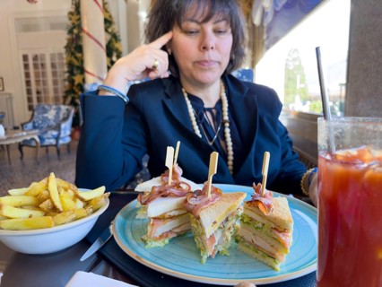 Elegant Woman Sitting Around a Table in Restaurant and Eating Club Sandwich with Bacon and French
