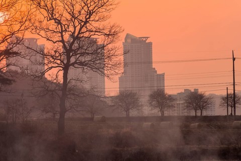 Smoke in the air at sunset obscures the view of apartments and trees and creates a halloween like