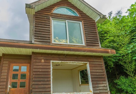 View of window on second story, front door and first floor window frame of abandoned house in