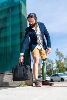 Vertical photo of a businessman with prosthetic leg leaving a laptop bag on the floor outdoors