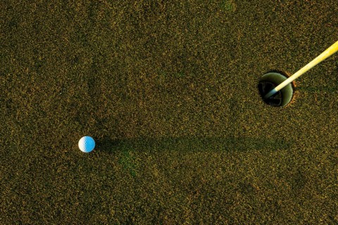 Golf Ball on the Grass with Shadow and Hole with Flag Pole on Putting Green on Golf Course in