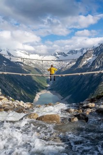 Mountaineer sitting on a suspension bridge over a mountain stream Alelebach, picturesque mountain