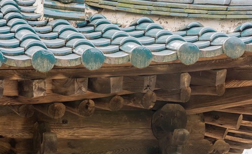 View of tiled roof and wooden beams of an abandoned, unused oriental pavilion in a woodland area in