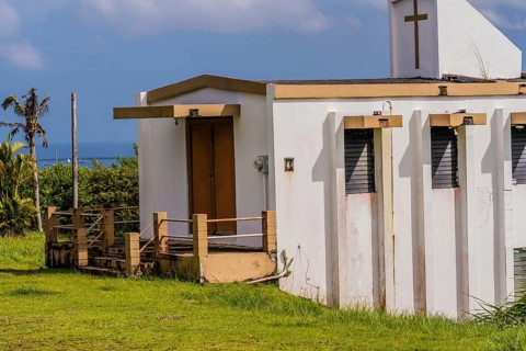 Side view of a small white country church sitting on a hillside in Guam with a view of the ocean