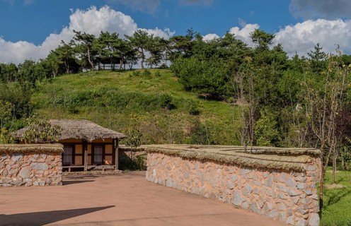 Old thatch roof building behind mud and stone wall at urban public park