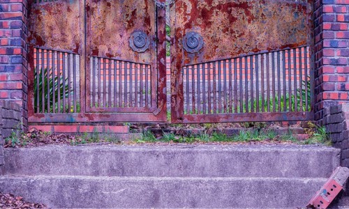View of stairs leading to a chained rusted gate with red brick columns on each side located at old