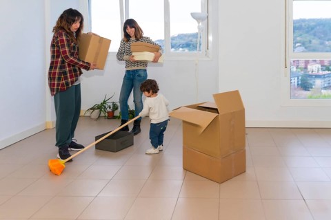 A little girl plays with a broom while her mothers move into a new house