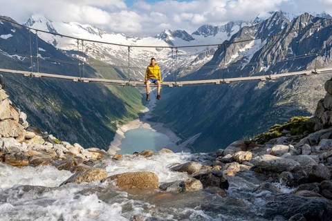 Mountaineer sitting on a suspension bridge over a mountain stream Alelebach, picturesque mountain