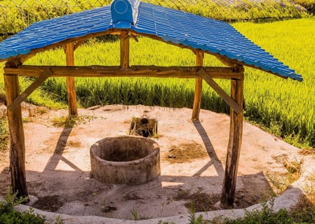 Concrete irrigation well under structure with blue metal roof at edge of rice paddy in rural