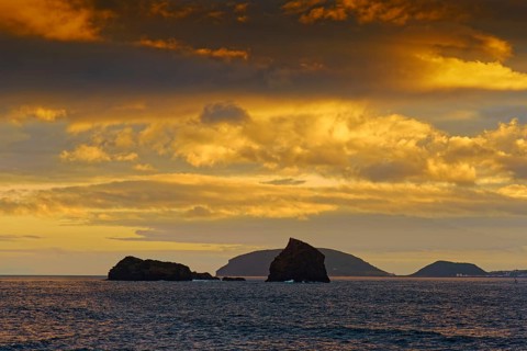 Sea view of the rocks Ilheu em Pe and Ilheu Deitado under an amber-coloured evening sky with