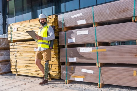 Engineer with prosthetic leg working outdoors with paperwork in a construction site leaning on a