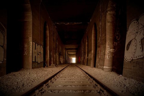 An abandoned railway tunnel, symmetrical with rails and side walls full of graffiti, former Rethel