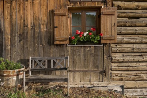Alpine hut with wooden bench and window with shutters and geraniums, Alpe di Siusi, South Tyrol,