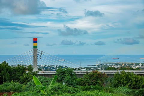 A highway with Mauritian emblem on pillar and a truck driving, surrounded by mountains and an