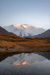 White glaciated and snowy mountain peak Pik Lenin at sunset, mountains reflected in a lake between