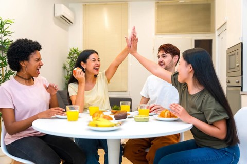 Multi-ethnic friends celebrating while high-fiving during breakfast together at home