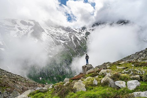 Mountaineer standing on a rock, cloudy mountain landscape with blooming alpine roses, view of rocky
