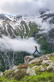 Mountaineer jumping from one rock to the next, cloudy mountain landscape with blooming alpine