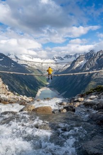 Mountaineer sitting on a suspension bridge over a mountain stream Alelebach, picturesque mountain
