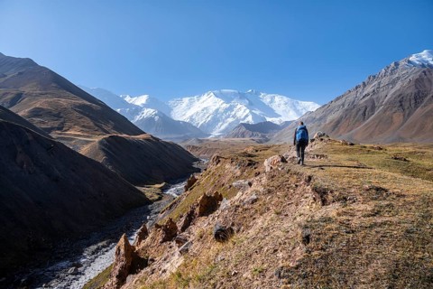 Hiker at the valley with river Achik Tash between high mountains, mountain landscape with peak Pik