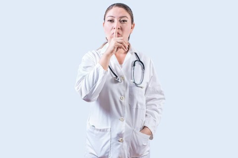 Female doctor making silence gesture isolated. Beautiful female doctor silencing and looking at the