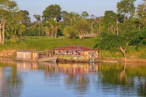 Wooden house and boat in the flooded forest along the Madeira River at sunset, Amazonas state,