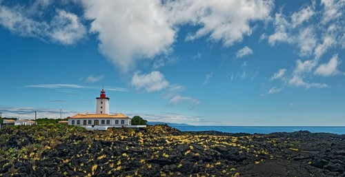 Wide lava flow with the striking lighthouse Farol da Ponta da Iha in front of a blue sky with white