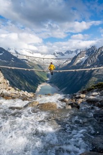 Mountaineer sitting on a suspension bridge over a mountain stream Alelebach, picturesque mountain