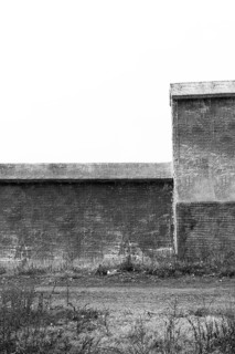 Black and white of small wire-frame and stucco building in countryside. Building has no window or