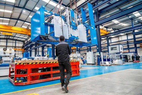 Worker using a crane to lift very heavy machinery in a factory