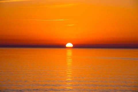 Intense, atmospheric sunset with bright orange-yellow sky over the Baltic Sea, reflection of the