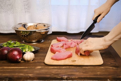 Female hands slicing raw pork fillet for ragout in the kitchen