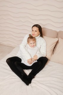 Family photo of pretty mother with long dark hair wearing knitted white sweater posing with her