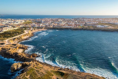 Drone view of waves break on rocky shores in town of Peniche, Portugal. Summer sunset haze, little