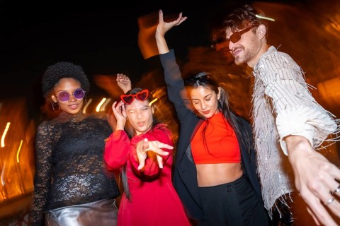 Night photo with flash and motion of fashion multi-ethnic friends dancing with elegant clothes in