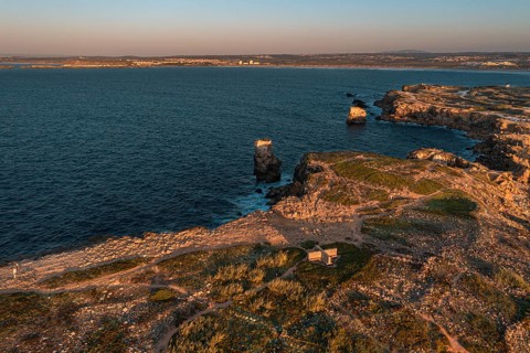 Bird's-eye view of sunset over ocean waves break on rocky shores, Peniche, Portugal. Summer sunset