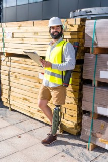 Vertical portrait of a smiley engineer with amputee leg working in a construction site