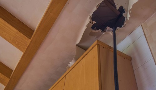 Large hole and torn wallpaper in ceiling above kitchen cabinets in abandoned house