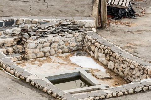 Remains of building foundation made of stone and concrete with square pool of water in center