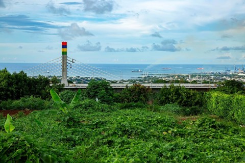 A highway with Mauritian emblem on pillar and a truck driving, surrounded by mountains and an