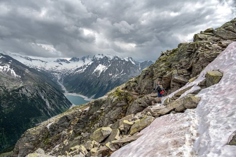 Mountaineer on hiking trail with snow, view of Schlegeisspeicher, glaciated rocky mountain peaks