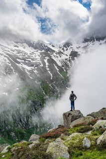 Mountaineer standing on a rock, cloudy mountain landscape with blooming alpine roses, view of rocky