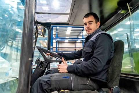 Male manual worker driving a forklift in a modern cnc logistic factory