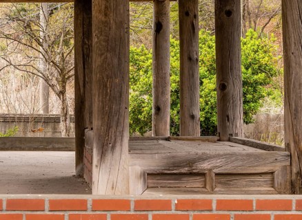 Inside view of old oriental style covered pavilion surrounded by a concrete wall in an overgrown