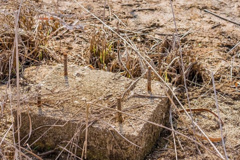 Concrete block with threaded metal bars that is part of building foundation in tall grass of dried